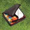 A folded picnic rug with a colourful checked design in a black carry bag, set on green grass.