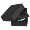 A silver compact mirror inside a black box, resting on a soft black cloth. The box has a minimalist design.