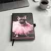 A notebook with a black cover featuring a pink tutu-wearing dog on the front. It includes a logo.