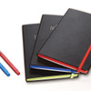 A set of three black bound journals with coloured elastic bands and pens in blue, red, and green.