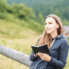 A woman holding a black Spectrum Pocket Notebook while sitting outdoors in a natural setting.