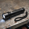 A black torch with a textured grip and a wrist strap, featuring a bright LED light at the front.