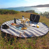 A round picnic rug with navy and white stripes, surrounded by snacks, a drink bottle, and a picnic bag.