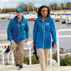 A blue rain jacket worn by a woman, paired with a blue cap and beige trousers, near a marina.