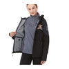 A woman wears a black softshell jacket open to reveal a grey interior. The jacket features a logo on the sleeve.
