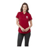 A women's short sleeve polo shirt in red, featuring a logo. The model is wearing it with dark jeans.