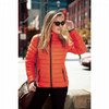 An orange puffer jacket worn by a woman, featuring zippered pockets and a sleek design, set against an urban background.