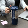 A drink bottle featuring a blue body and decorative patterned sleeve, with a handle and straw, resting on a table.