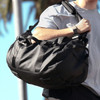 A black duffel bag with sturdy straps and textured detailing, being held by a person.