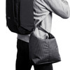 A cooler bag in a grid pattern, featuring a shoulder strap, being carried on the side of a person with a backpack.
