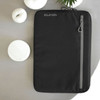 A black laptop sleeve featuring a front zipper pocket and a logo. Set against a neutral background with candles.