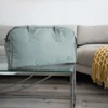 A green duffle bag sits on a glass table, with a sofa and blanket in the background. The bag has handles and a logo.