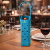 A drink bottle bag in bright blue, featuring a handle and holes, displayed on a dining table with wine glasses.