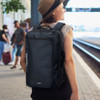 A black convertible travel backpack with a carry handle and shoulder straps, worn on a person's back at a train station.