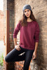 A maroon jumper with long sleeves worn by a model, paired with a grey beanie, set against a brick wall.