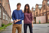 A blue and a maroon jumper worn by a man and a woman standing in an urban setting with industrial buildings.