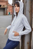 A grey ladies hoodie with a zip and pockets, worn by a model against a metal structure.