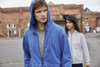 A blue zip hoodie and a grey zip hoodie worn by a man and a woman in an outdoor urban setting. Both hoodies have logos.
