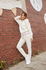 A cream hoodie with a pink waistband, featuring a logo, worn with matching joggers against a brick wall backdrop.