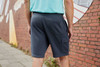 Men's lounge shorts in grey with a pocket, displayed from the back against a brick wall background.