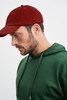 A man wearing a green hooded sweatshirt and a maroon cap, facing sideways. The cap has a logo.