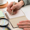 A Natural Pocket Rocket Notebook with a pen, placed on a map and accompanied by a magnifying glass and sticky notes.