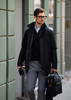 A black jacket worn over a dark sweater, paired with grey trousers and a stylish bag, featuring a logo.