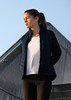 A soft shell jacket in navy, worn by a woman, features a zip front and a sleek design. It has branding on it.