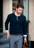 A navy Brighton O-Neck men's knit jumper with a white collared shirt underneath, paired with grey trousers and accessories.