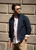 A navy jacket worn over a light pink shirt, modelled by a man with sunglasses against a textured wall.