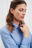 A light blue button-up shirt with a collar, featuring a model showcasing the garment. The shirt has long sleeves and a logo.