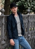 A man in a navy Davenport jacket stands by an ornate fence, wearing a grey shirt and jeans, with a cap.