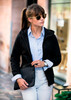 A black women's jacket is worn with a collared shirt. The model accessorises with sunglasses and holds a black clutch.