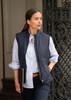 A navy women's vest is worn over a light blue shirt, paired with dark pants and a belt. A logo is visible on the vest.
