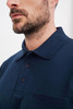 A navy blue polo shirt featuring a pocket and a classic collar, with a three-button placket and branding.