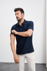 A navy polo shirt with a short sleeve, featuring a pocket and a brand logo. Model adjusts the sleeve.