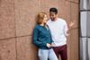 A teal jumper worn by a woman and a white jumper worn by a man, both smiling against a textured wall.