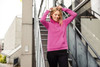 A pink ladies hoodie with a drawstring hood, worn by a woman, against an urban backdrop of stairs and buildings.