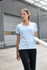 A light blue women's work t-shirt is displayed on a model with black pants, set in an industrial environment.