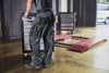 Workwear pants in black, featuring pockets, being worn by a person moving a tool trolley in an industrial setting.