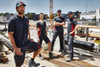 Four individuals wearing black and red men's workwear polos stand on a construction site surrounded by building materials.