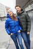 A blue padded jacket worn by a woman and a green padded jacket worn by a man, both smiling outdoors.