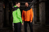 A green and black ladies rain jacket and an orange and black men's rain jacket are displayed together in an industrial setting.