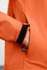 An orange ladies softshell jacket featuring a side pocket and adjustable cuff with a hook and loop fastener.