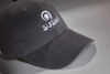 A black brushed 6 panel cap featuring an embroidered logo. The cap has a curved brim and adjustable back.