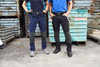 Two individuals wearing workwear pants in navy and black, standing against a textured background of metal containers.