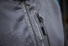 A close-up of a grey hardshell workwear jacket featuring a zip and water droplets on the fabric, with a logo present.