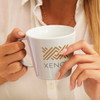 A coffee mug in pale grey featuring a logo and a person holding it with light-coloured nails.