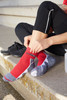 Sport socks in red with grey accents, featuring a logo, being worn by a person seated on a step.