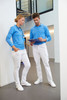 A woman in blue and a man in blue shirts wearing white stretch pants stand together indoors, reviewing a tablet.
